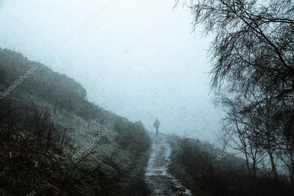 A silhouette of a man walking on path in the countryside, on a spooky foggy winters day. With a grunge, vintage muted edit.
