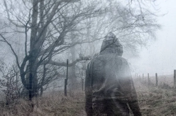 気分の悪い霧の冬の日に田舎道でフードを被った男の芸術的な 二重の露出 グランジ ぼやけた編集で — ストック写真