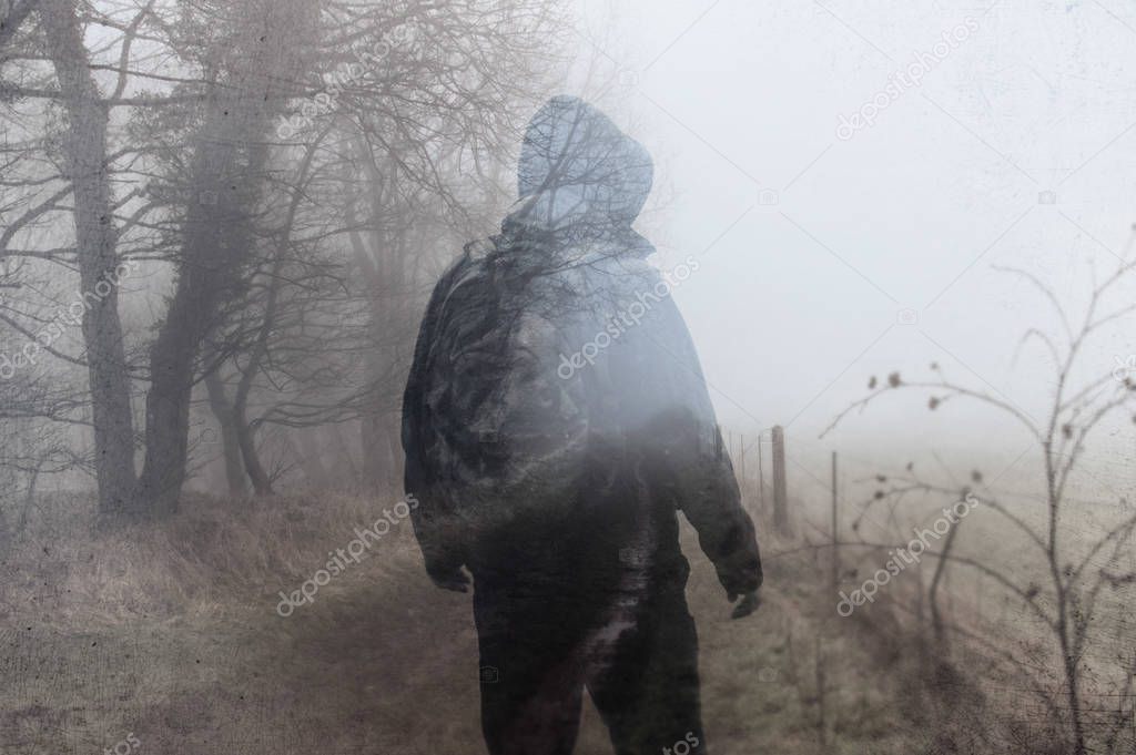 An artistic, double exposure of a hooded man on a country path on a moody foggy winters day. With a grunge, blurred edit.