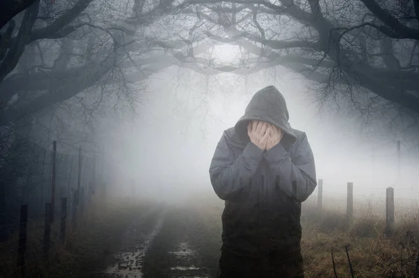 彼の手に頭を保持しているフード付きの人物の芸術的な二重露出 霧の多い冬の日に気分の悪い田舎道を重ねて — ストック写真