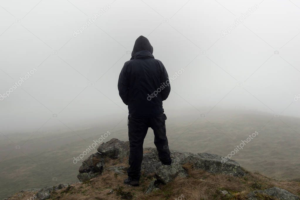 Looking at the back of a hooded figure looking out on a moody foggy winters day.