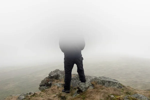 Looking at the back of a hooded figure looking out on a moody foggy winters day. With his head disappearing into the fog.