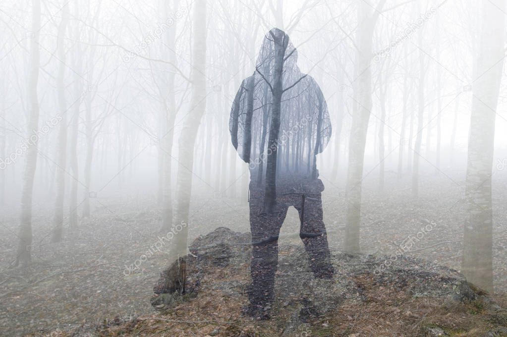 A double exposure looking at the back of a hooded figure looking out over a moody forest on a winters day.