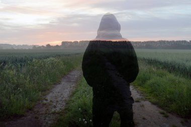 Sisli bir yaz gün doğumu, bir alan üzerinden giden bir ülke yolu üzerinde katmanlı bir kapüşonlu rakam, bir çift pozlama