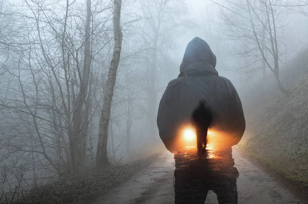 A double exposure concept. A hooded figure looking at a silhouette of a man in front of car headlights. On a spooky forest track on a misty winters evening.
