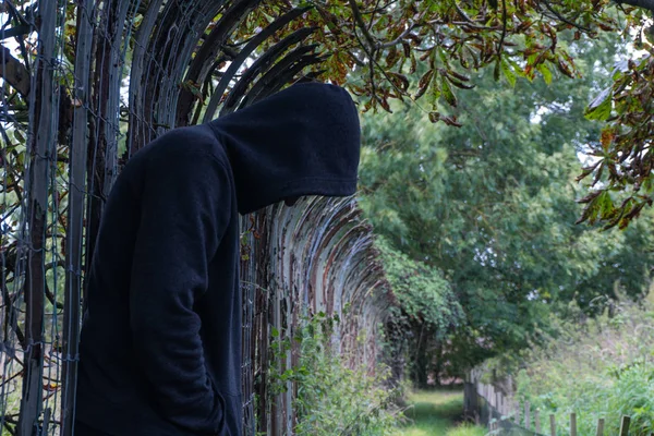 A hooded man, looking down, depressed and alone. standing next t