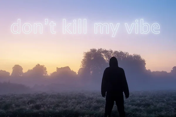 A cool hipster motivation phrase. A hooded figure outdoors looking at a sunrise with the phrase \