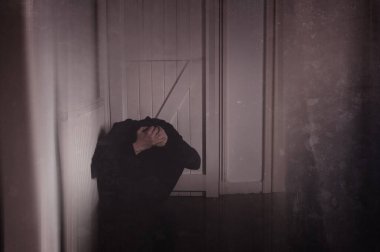 Kafasını elinde tutan bir adam, odanın bir köşesinde oturuyor. Eski, grunge, bulanık bir düzenleme ile 