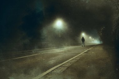 Gecenin bir yarısı yolun ortasında duran kapüşonlu bir figür. Bulanık, soyut, grunge bir düzenleme ile