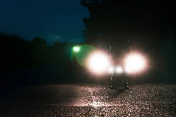 道路の真ん中に立って車のヘッドライトに対してシルエットの男 — ストック写真