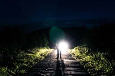 Gecenin bir yarısı arabanın farlarına dayanmış, yolun ortasında duran kapüşonlu gizemli bir adam.