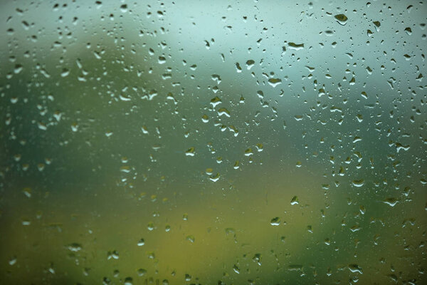 Rainy glass on the background of the autumn park! Water drops on glass and blurred texture in the background.