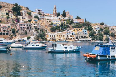 Symi Adası, Yunanistan - Haziran 2018 yaklaşık: güneşli bir günde, Yunanistan ve arka plan üzerinde renkli evleri sahil Symi Adası ve tepeler, berrak mavi suları tekneler float.