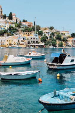 Symi Adası, Yunanistan - Haziran 2018 yaklaşık: güneşli bir günde, Yunanistan ve arka plan üzerinde renkli evleri sahil Symi Adası ve tepeler, berrak mavi suları tekneler float.