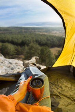 Çadırdan görüntüleyin. Serin yolculuk. Bir çadırda oturan bir kız elini gösterir gibi bir thermocup sahiptir. Dağlarda çadır görünümden. Gerçek fotoğraf hiking.