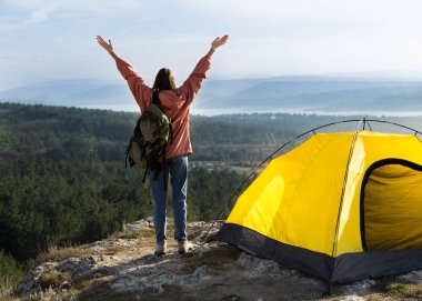 Kız ellerini gökyüzüne karşı dağlar, ormanlar, göller fon yükseltir. Yakınlarda bir çadır var. Gerçek fotoğraf hiking.