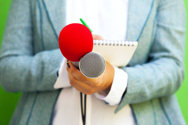 Женщина-репортер на пресс-конференции, пишет заметки, держит микрофон