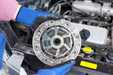 Otomatik mekanik koruyucu iş eldiven giymiş eski debriyaj disk üzerinde bir araba motoru tutar.