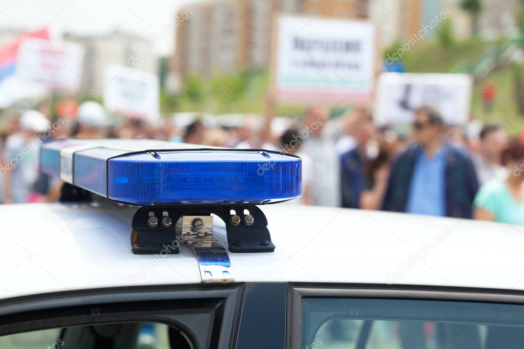 Police car flashing lights in focus, blurred protesters in the background
