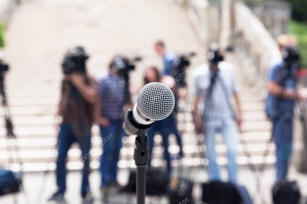 Microphone in focus against blurred camera operators and reporters at press conference