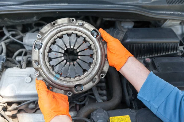 Auto mechanic wearing protective work gloves holding used clutch pressure plate above a car engine — Stock Photo, Image