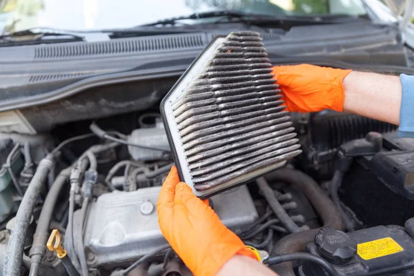 Auto mécanicien portant des gants de travail de protection tenant filtre à air sale au-dessus d'un moteur de voiture — Photo