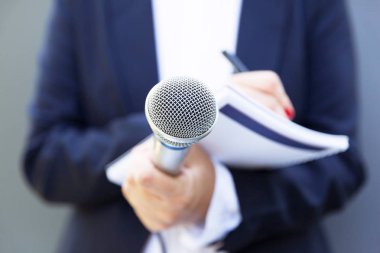 Basın konferansında ya da medya etkinliğinde kadın gazeteci, notlar yazma, mikrofon tutma