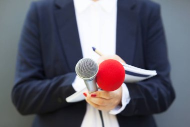 Basın konferansında kadın gazeteci, notlar yazıyor, mikrofon tutuyor.