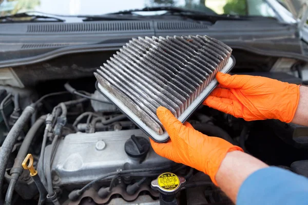 Auto mécanicien portant des gants de travail de protection tenant filtre à air sale au-dessus d'un moteur de voiture — Photo