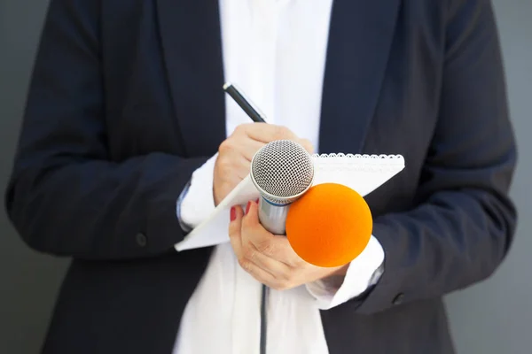 Journaliste féminine lors d'une conférence de presse ou d'un événement médiatique, écrivant des notes, tenant un microphone — Photo