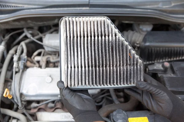 Auto mecânico usando luvas de trabalho de proteção segurando sujo filtro de ar usado acima de um motor de carro — Fotografia de Stock