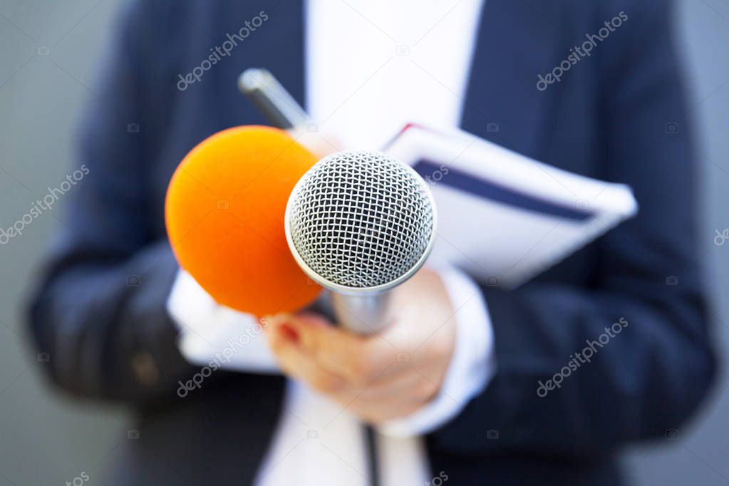 Female journalist at news conference or media event, writing notes, holding microphone
