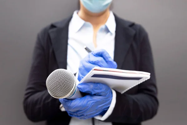 Female journalist at news conference or media event, writing notes, holding microphone during COVID-19 virus pandemic