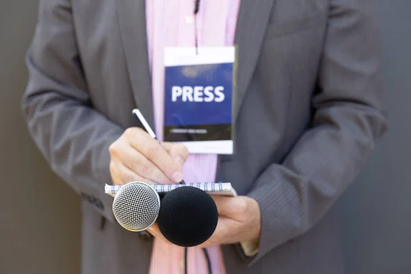 Reporter at press conference or media event, writing notes, holding microphone