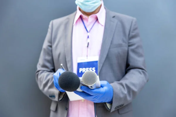 Journalist at news conference or media event wearing protective gloves and face mask against coronavirus COVID-19 disease holding microphone writing notes during virus pandemic