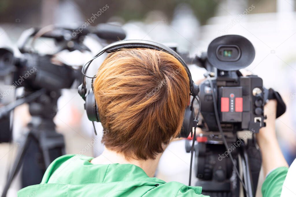 Camerawoman at work during news conference or media event filming with video camera