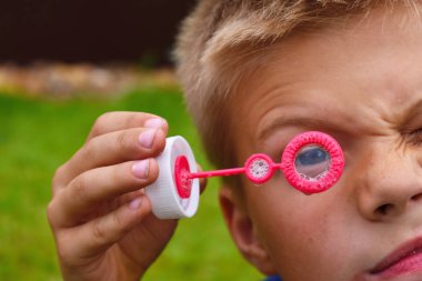 Çocuk sabun köpüğünün halkasının içinden bakar. Komik kişi çocuk.