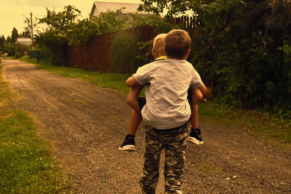 Летом братья играют на улице. Мальчик несет другого мальчика на — стоковое фото