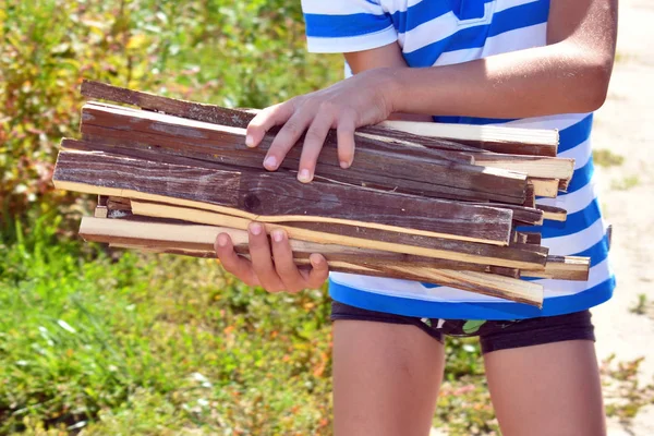 The boy holds firewood for fire in hand in summer. Active childr — Stock Photo, Image