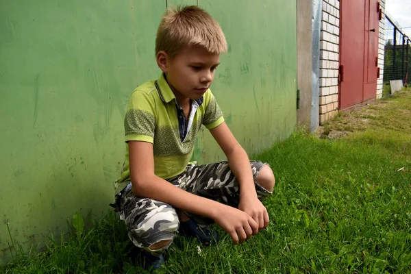 Обиженный и злой мальчик сидит у стены летом на улице — стоковое фото