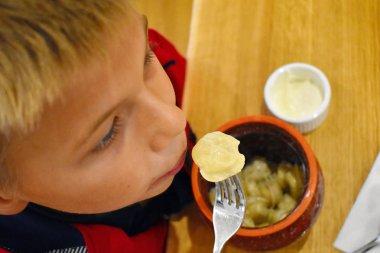 Çocuk seramik bir tencerede pişmiş pelmeni yiyor. 