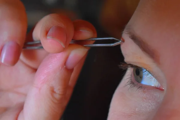 Pinças menina puxa fora de uma sobrancelha um close-up . — Fotografia de Stock