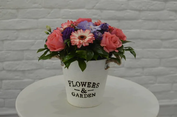 Beautiful lovely bouquet for flower shop. Beautiful bouquet of colorful flowers in packing on white table against the background of brick white wall.  No people.  Close-up.  Concept of flower shop.  Bouquet for catalog.