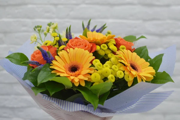 Beautiful bouquet for flower shop. Beautiful bouquet of colorful flowers in packing on white table against the background of brick white wall.  No people.  Close-up.  Concept of flower shop.  Bouquet for catalog.