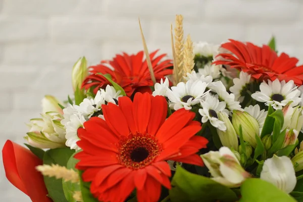 Beautiful lovely bouquet for flower shop. Beautiful bouquet of colorful flowers in packing on white table against the background of brick white wall.  No people.  Close-up.  Concept of flower shop.