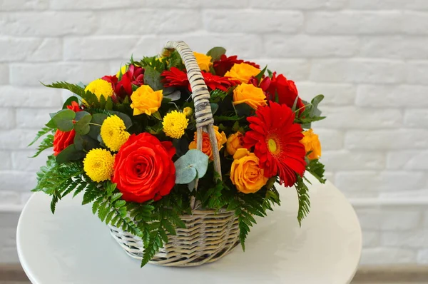 Beautiful flower basket on a table. Beautiful bouquet of colorful flowers in  basket on  table against the background of  brick white wall. No people. Close up. Concept of flower shop. Composition for the catalog.