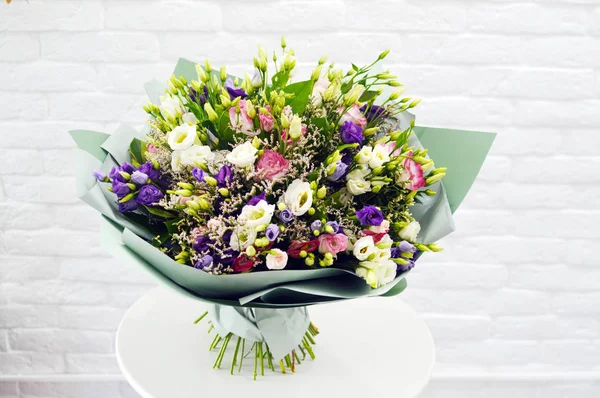 Beautiful lovely bouquet for flower shop. Beautiful bouquet of wind flowers in packing on white table against the background of brick white wall.  No people.  Close-up.  Concept of flower shop.  Bouquet for catalog.