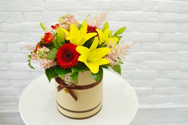 Spring bouquet of flowers in stylish hat box on white table. Beautiful bouquet of colorful flowers in hat box.  Concept of flower salon.  Photo for flower catalog or website. Work of professional florist.  No people. Light background.