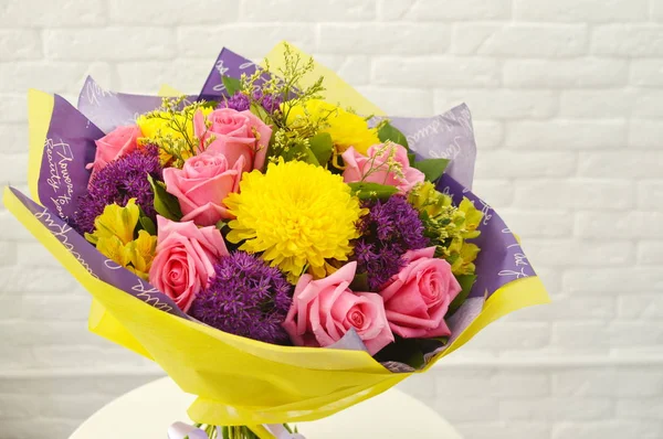 Mix of summer flowers bouquet for the wedding. Beautiful bouquet of colorful flowers in packing on white table against the background of brick white wall.  No people.  Close-up.  Concept of flower shop.  Bouquet for catalog.