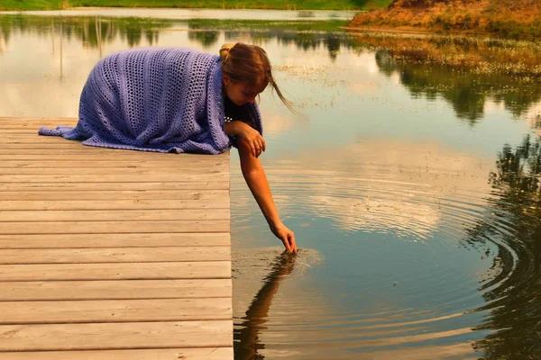 Girl drinks water from the lake. Woman on a pier in a blue knitted plaid.